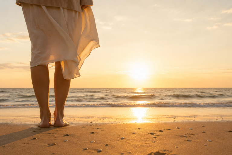 Ankommen Barfüßige Frau steht am Strand und blickt auf das Meer, Sonnenuntergang spiegelt sich im nassen Sand