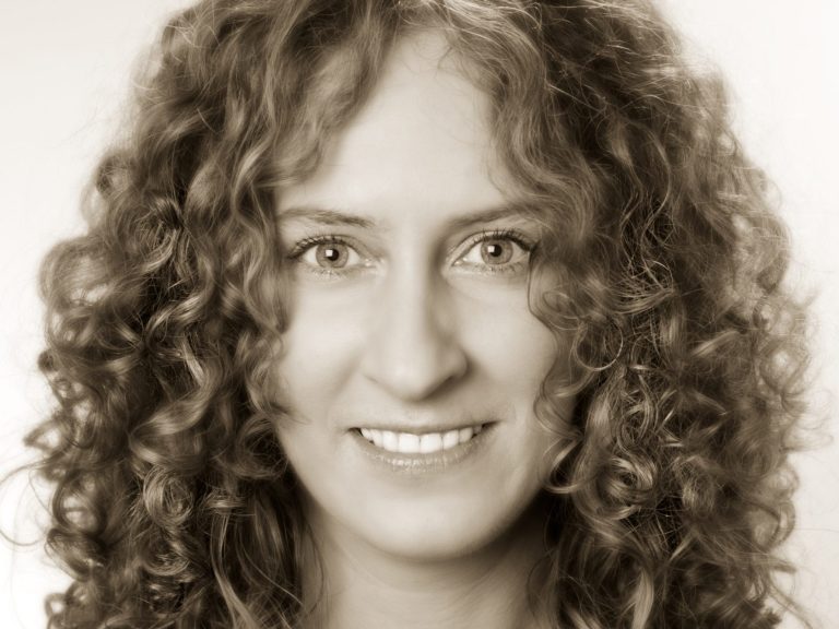 orträt von Yvonne Schwarz, Coaching und Energetic Health, warmes Sepia-Schwarz-Weiß-Foto mit lockigem Haar und offenem Lächeln